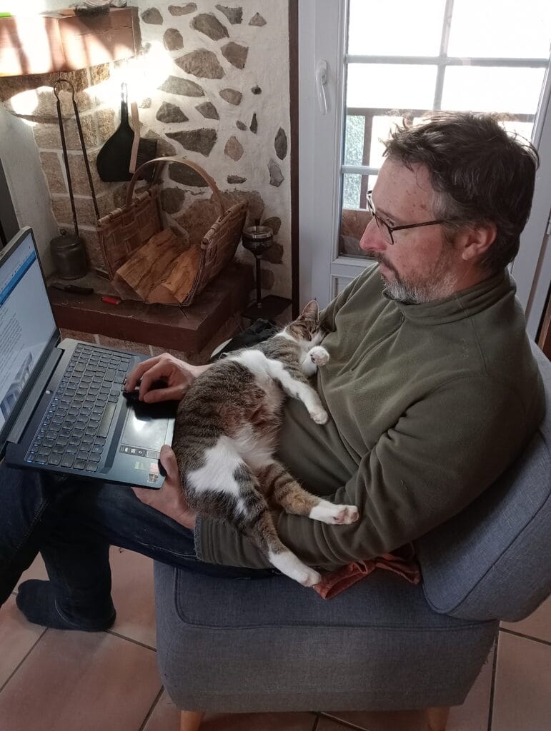Stéphane Péna essaie de bosser sur son ordinateur portable, malgré son chat qui claque une sieste dans ses bras.